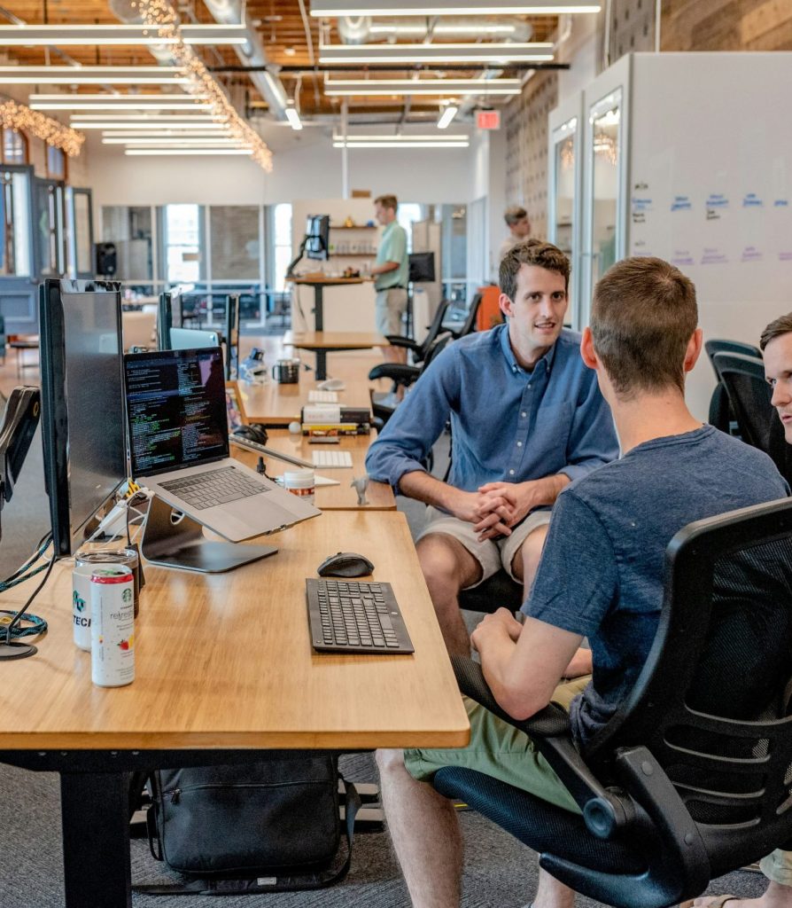 Drei Männer sitzen auf Stühlen neben Tischen