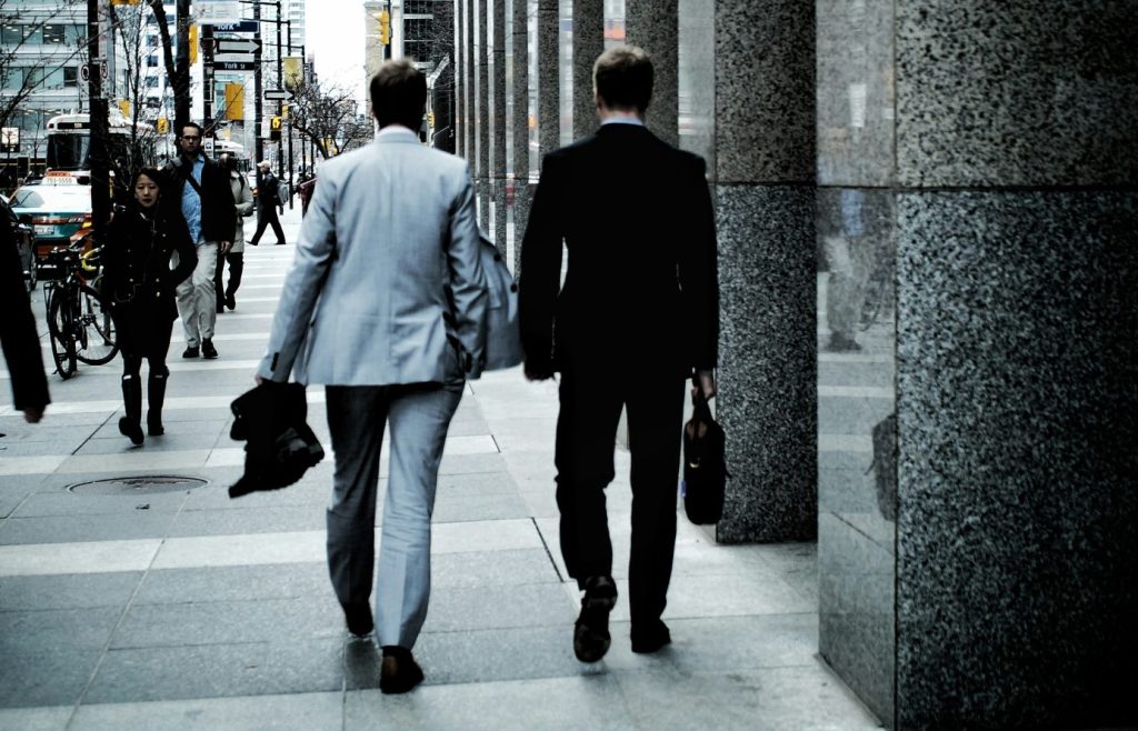 Menschen, die tagsüber auf dem Gehweg neben der Straße mit Fahrzeugen und Hochhäusern spazieren gehen.